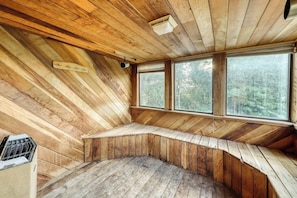 Ein Holzblockhaus-Interieur mit einer gebogenen Sitzbank, großen Fenstern und einem Deckenlüfter.