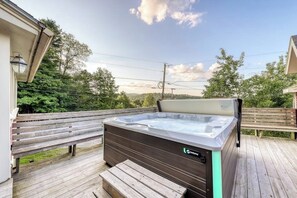 Ein Whirlpool auf einer Holterrasse mit einer Bank, umgeben von Bäumen und blauem Himmel.