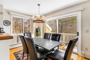 A dining area with a table and chairs, a chandelier, large windows, and a view of trees. - Beautiful Stowe getaway w/ shared pool/hot tub, balcony & wood-burning fireplace (Stowe)