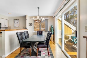A dining area with a table and chairs, a chandelier, and a view through large windows. - Beautiful Stowe getaway w/ shared pool/hot tub, balcony & wood-burning fireplace (Stowe)