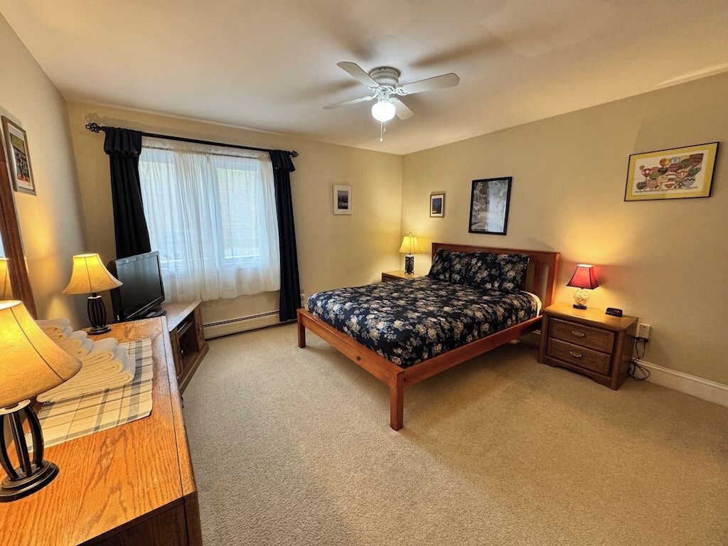 A bedroom with a bed, bedside tables, lamps, a ceiling fan, and a window with curtains.
