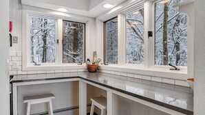 Ett kök med en vit bänkskiva, två vita barstolar och fönster med frostat glas.