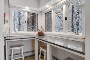 A kitchen with a white countertop, two white stools, and windows with frosted glass. - Three-Level House Near Skiing w/Free WiFi, Private Hot Tub, Gas Fireplace (Stowe)