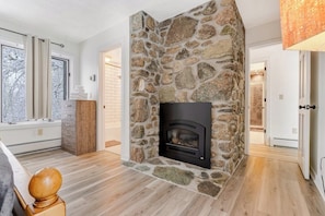 A stone fireplace, wooden flooring, a window with curtains, and a door leading to another room. - Three-Level House Near Skiing w/Free WiFi, Private Hot Tub, Gas Fireplace (Stowe)
