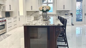 A modern kitchen with white cabinetry, a marble countertop, and a central island with a vase of flowers. - 7,000 sqft Luxury Countryside Mansion on 1 acre estate lot, swimming pool 12 par (York)