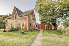 A two-story house with a front porch, a small attached garage, and a large tree in the yard. - Quaint Getaway Near Town W/ Hot Tub, Large Deck, Sauna & Free WiFi (Stowe)