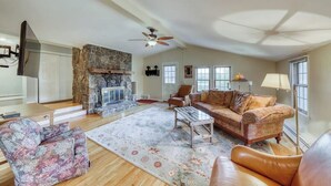 A spacious living room with a stone fireplace, leather sofas, a coffee table, and a large window. - Adorable Getaway w/ Free WiFi, Full Kitchen, & Two Decks (Stowe)