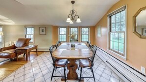 A dining room with a large wooden table, six chairs, a chandelier, and large windows. - Adorable Getaway w/ Free WiFi, Full Kitchen, & Two Decks (Stowe)
