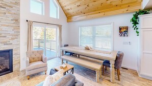 A spacious living room with a fireplace, a dining table, and a balcony. - Waterfront home on Lake Champlain with pool, hot tub, dock, kayak & canoe (North Hero)
