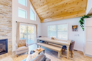 A spacious living room with a fireplace, a dining table, and a balcony. - Waterfront home on Lake Champlain with pool, hot tub, dock, kayak & canoe (North Hero)