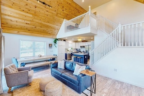A spacious living area with a wooden ceiling, a staircase, a kitchen, and a seating area with a sofa and armchairs. - Waterfront home on Lake Champlain with pool, hot tub, dock, kayak & canoe (North Hero)