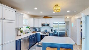 A modern kitchen with white cabinets, stainless steel appliances, and a central island with stools. - Waterfront home on Lake Champlain with pool, hot tub, dock, kayak & canoe (North Hero)