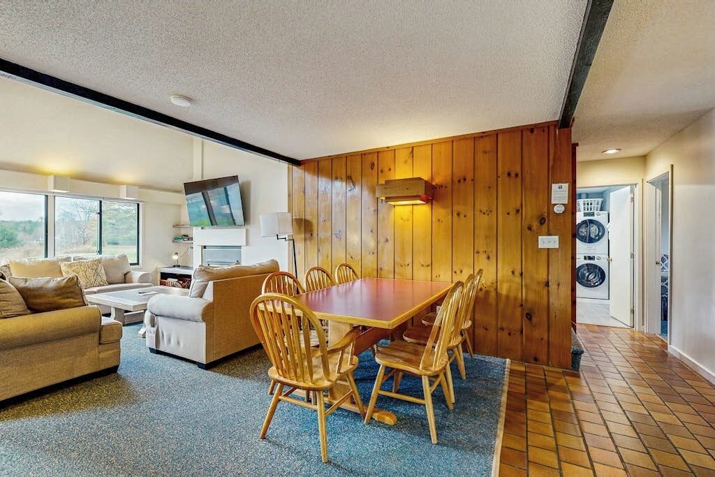 A room with a dining table, chairs, a sofa, a TV, and a washing machine.