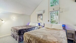 A bedroom with two beds, a window, a nightstand, and a wall-mounted air conditioner. - Golf course-front condo with loft, indoor & outdoor pools, hot tub, & game room (Stowe)
