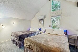 A bedroom with two beds, a window, a nightstand, and a wall-mounted air conditioner. - Golf course-front condo with loft, indoor & outdoor pools, hot tub, & game room (Stowe)