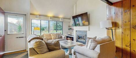 A modern living room with a fireplace, two sofas, a coffee table, and a TV mounted on the wall.