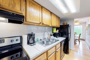 A kitchen with wooden cabinets, a black stove, a sink, and a refrigerator. - Condo with balcony, washer/dryer, & shared indoor pool/hot tub (Stowe)