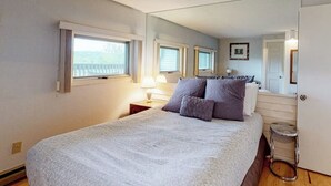 Et soveværelse med en seng, et natbord, en lampe, et spejl og et vindue med persienner.