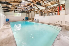Ein Innenpool mit Betonboden, Holzbalken und einer weißen Wand mit einem Fenster.