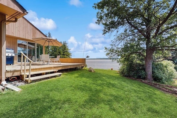 A wooden deck with outdoor furniture, a grill, and a view of a body of water. - Dog-friendly, home on Lake Champlain with panoramic views of the Green Mountains (North Hero)