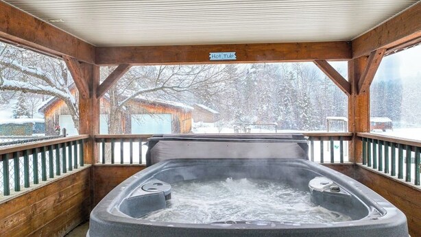 Een hottub in een houten hutje met uitzicht op met sneeuw bedekte bomen.