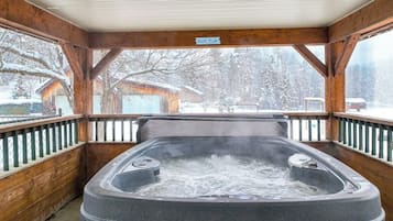 Ein Whirlpool in einer Holzhütte mit Blick auf schneebedeckte Bäume.