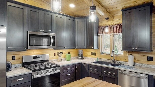 A modern kitchen with dark cabinets, stainless appliances, and a wooden island. - Enchanting dog-friendly cabin with fireplace, hot tub & washer/dryer (Morrisville)