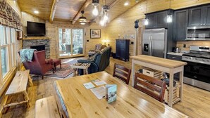 A wooden cabin interior with a dining area, kitchen, and seating. - Enchanting dog-friendly cabin with fireplace, hot tub & washer/dryer (Morrisville)