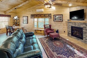 L’intérieur d’une cabane en rondins, avec un canapé en cuir, une cheminée, un téléviseur et un coin repas.