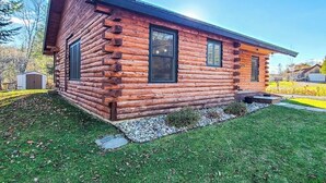 A log cabin with a front porch, a small front yard, and a clear sky. - Enchanting dog-friendly cabin with fireplace, hot tub & washer/dryer (Morrisville)