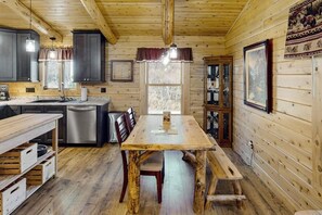 L’intérieur d’un chalet en bois comprend une table à manger, des chaises, un coin cuisine et une fenêtre.