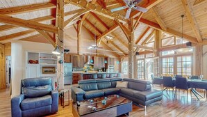 A spacious living area with a wooden ceiling, a large sectional sofa, a coffee table, and a dining area with chairs. - Private mountain retreat with a game room, home theater, & jetted tub (Underhill)