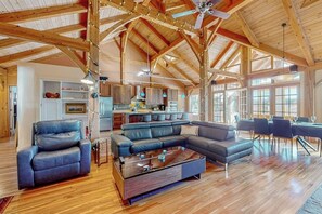A spacious living area with a wooden ceiling, a large sectional sofa, a coffee table, and a dining area with chairs. - Private mountain retreat with a game room, home theater, & jetted tub (Underhill)