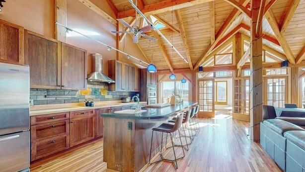 A spacious kitchen with wooden cabinets, a central island with bar stools, and a large window providing natural light. - Private mountain retreat with a game room, home theater, & jetted tub (Underhill)