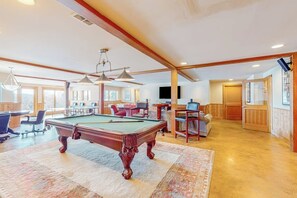 Una habitación amplia con mesa de billar, asientos cómodos y un gran ventanal que proporciona luz natural.
