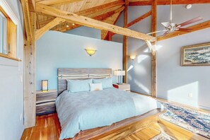 Un dormitorio con techo de madera, una cama con colcha azul claro, dos lámparas de noche y un ventilador de techo.