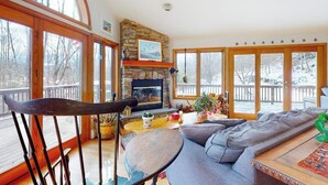 Una sala de estar acogedora con chimenea de piedra, ventanas amplias y una terraza de madera.