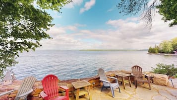 Une terrasse au bord du lac, avec des fauteuils Adirondack et une table en bois.