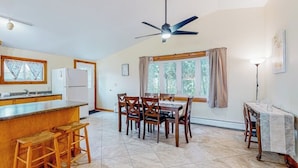 Une cuisine dotée d’un îlot central, un coin repas avec une table et des chaises, un ventilateur de plafond et une fenêtre avec des rideaux.