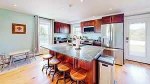 A modern kitchen with a central island, bar stools, stainless steel appliances, and a dining area with a bench and chairs.