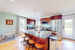 A modern kitchen with a central island, bar stools, stainless steel appliances, and a dining area with a bench and chairs.