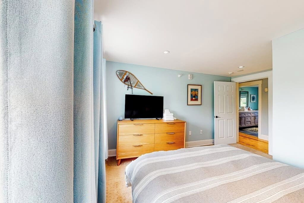 A bedroom with a bed, a dresser, a television on top, and a door leading to another room.
