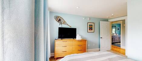 A bedroom with a bed, a dresser, a television on top, and a door leading to another room.