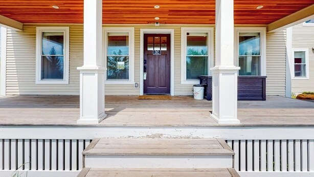 A house with a wooden deck, a front porch with columns, and a dark front door.