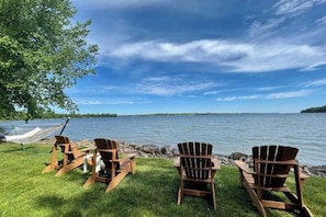 Un cadre idyllique au bord du lac, avec trois fauteuils Adirondack en bois et un hamac installés sur une pelouse.