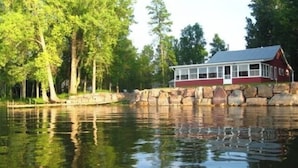 A lakeside cabin with a stone wall, surrounded by trees.