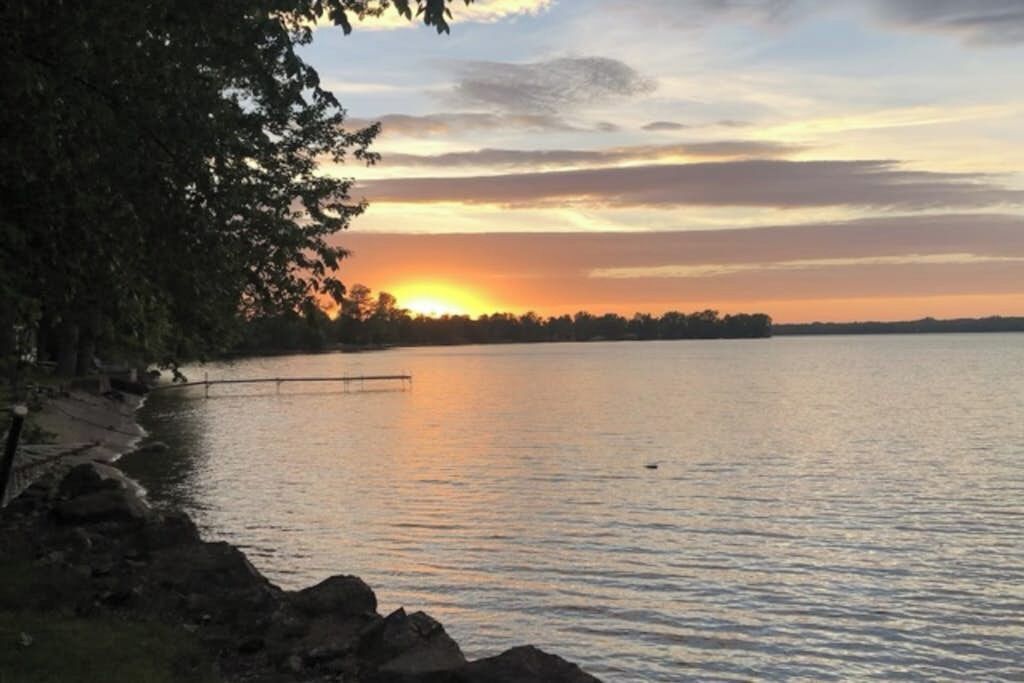 Ein ruhiger See bei Sonnenuntergang mit einer Anlegestelle und felsigem Ufer.