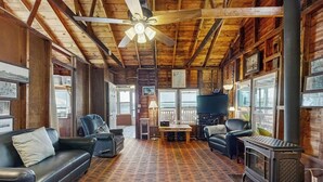 A cozy cabin interior with a wooden ceiling, a fireplace, a television, and a dining area.