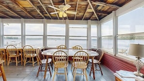 A covered dining area with wooden chairs, a table, and a ceiling fan.