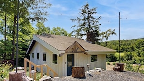 A small wooden cabin with a sloped roof, a front door, and a small porch area. - Riverfront house w/ valley & distant mountain views, fireplace, w/d, wifi (Stowe)